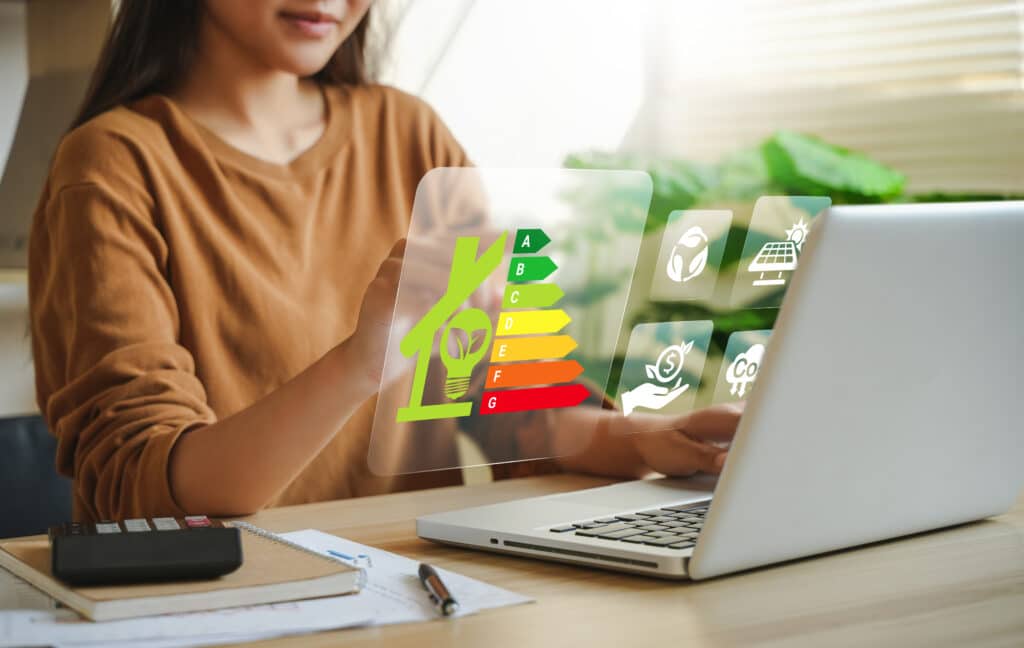 Efficacité Énergétique Maison : Durabilité et Économie Verte Femme interagit avec une interface holographique affichant l'efficacité énergétique (A-G) d'une maison. Icônes de durabilité, solaire, économie verte et empreinte carbone.