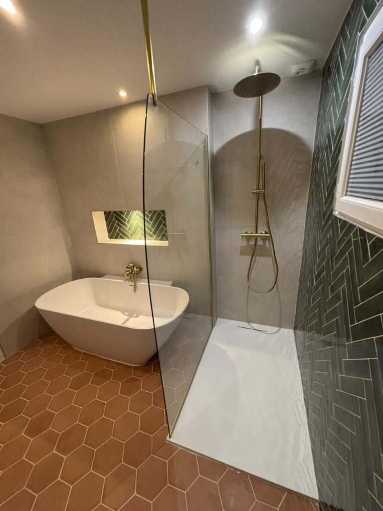 Salle de bain moderne avec baignoire îlot, douche à l'italienne, robinetterie laiton brossé, et carrelage hexagonal terre cuite.