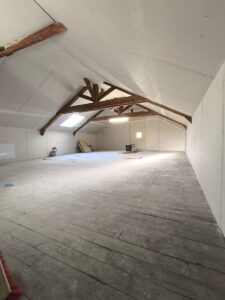 Aménagement de combles avec charpente bois apparente et plaques de plâtre prêtes pour la finition.