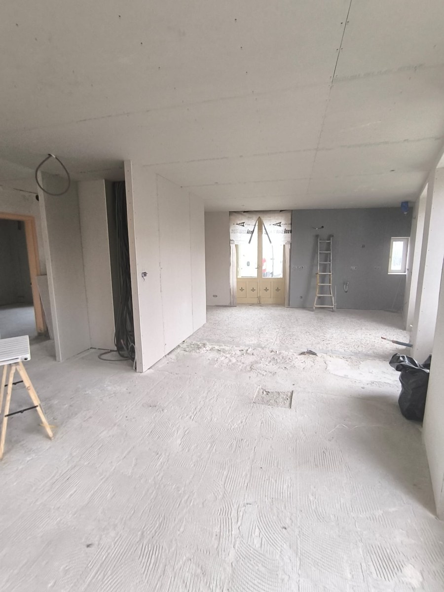 Chantier de rénovation avec plaques de plâtre au plafond, cloisons sèches et sol brut en béton.
