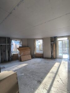Chantier de rénovation avec plaques de plâtre, isolant Knauf et Gutex, sol brut et porte-fenêtre ouverte.