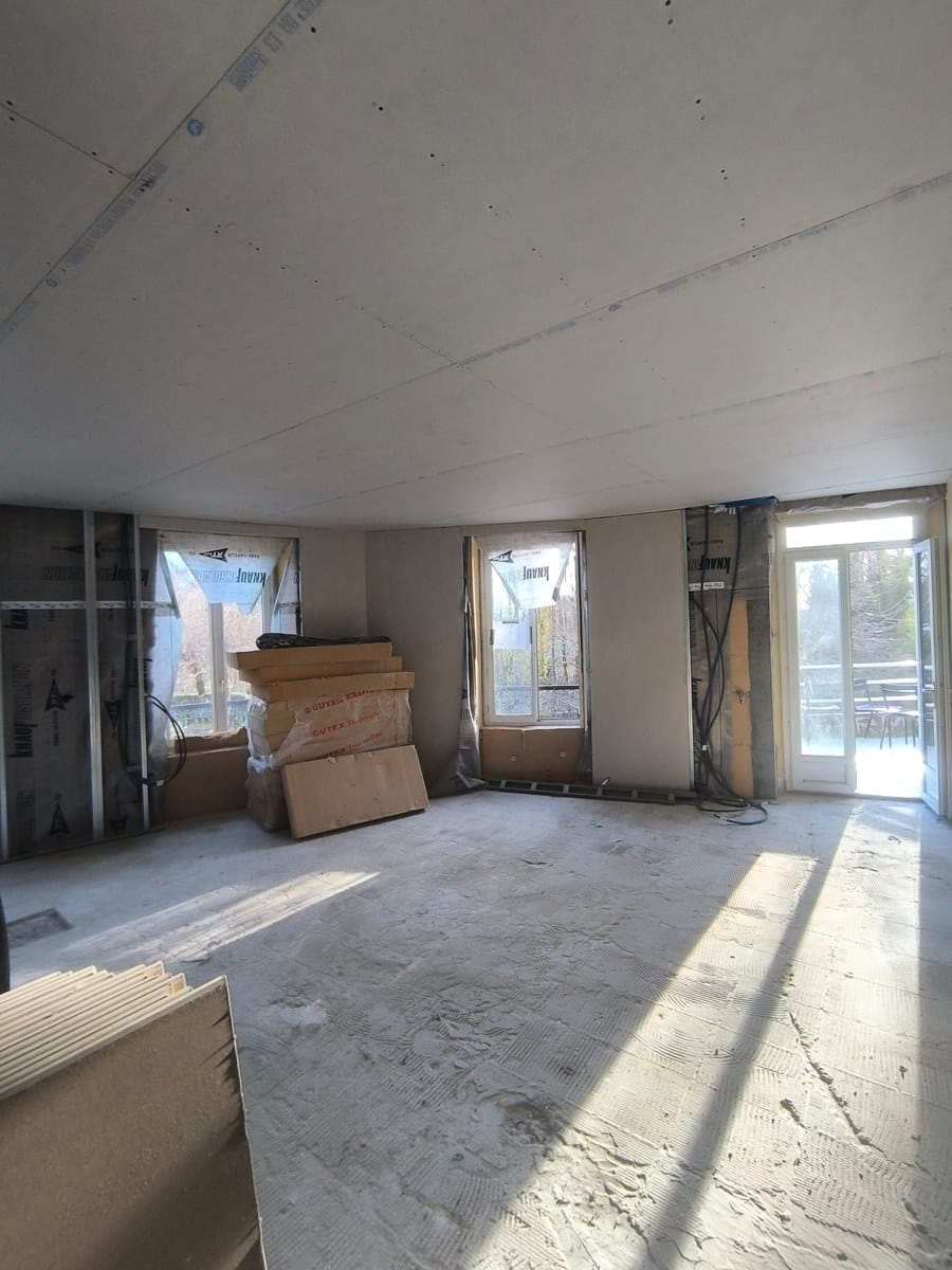 Chantier de rénovation avec plaques de plâtre, isolant Knauf et Gutex, sol brut et porte-fenêtre ouverte.