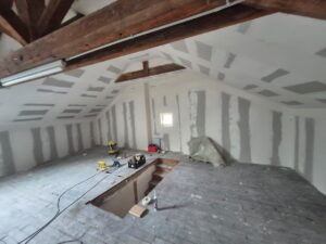Rénovation de combles : plaques de plâtre posées, poutres apparentes et outils au sol.