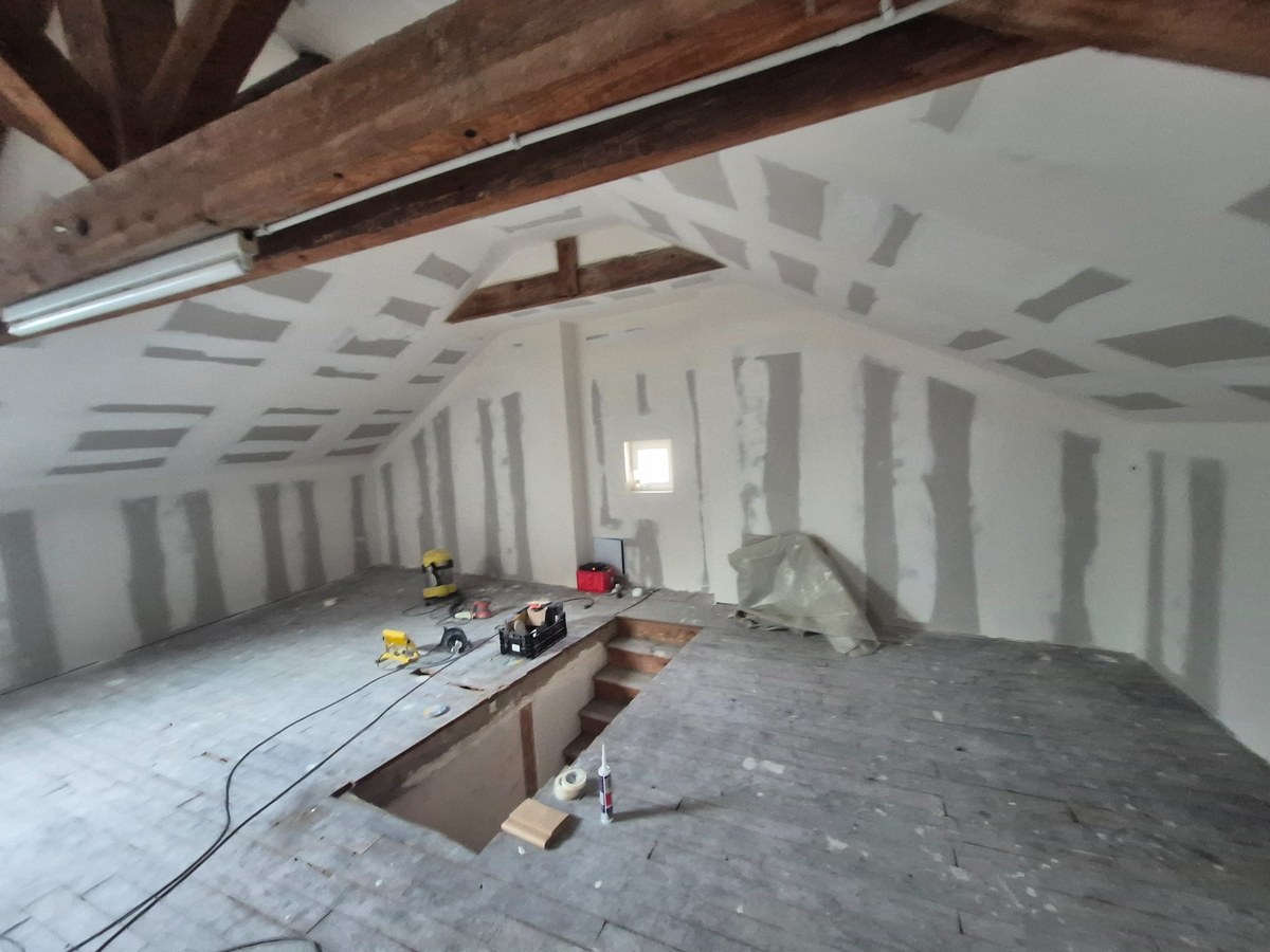 Rénovation de combles : plaques de plâtre posées, poutres apparentes et outils au sol.