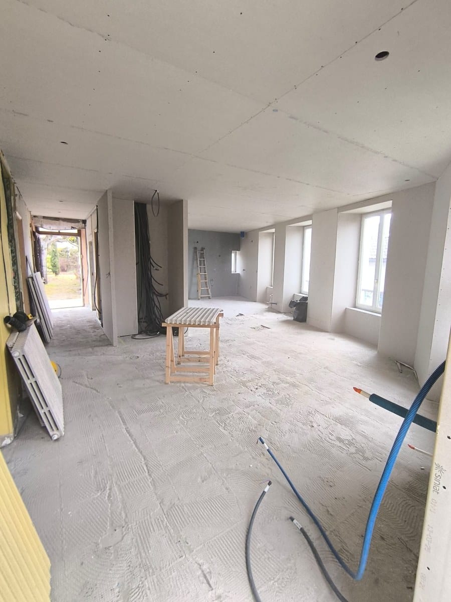 Pièce en rénovation avec plaques de plâtre au plafond, sol en béton brut et câblage électrique visible.