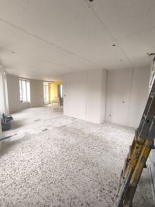 Intérieur en rénovation avec plaques de plâtre au plafond et murs, sol en terrazzo et échelle de chantier.