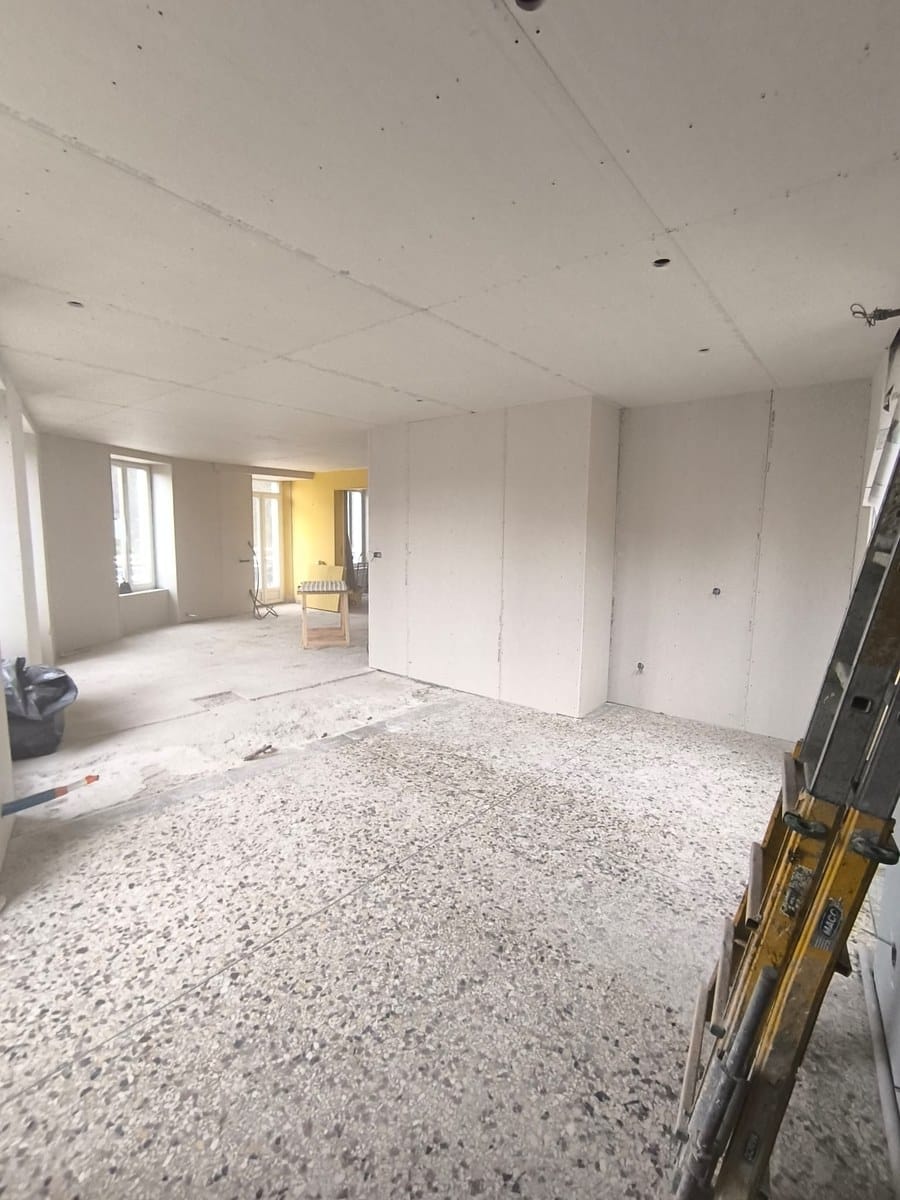 Intérieur en rénovation avec plaques de plâtre au plafond et murs, sol en terrazzo et échelle de chantier.