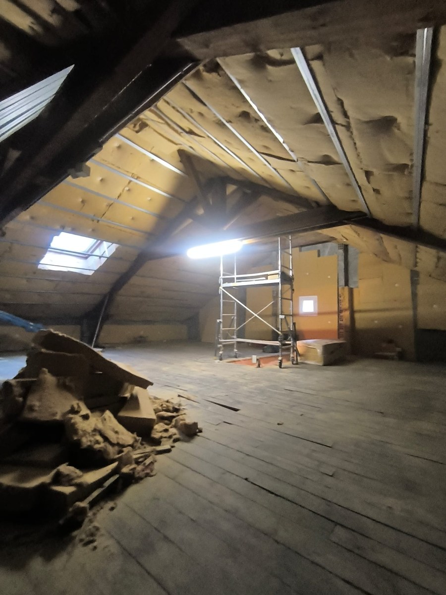 Combles en rénovation : isolation sous toiture, échafaudage central et charpente bois apparente.