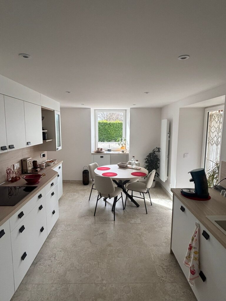 Cuisine moderne blanche et bois avec table de salle à manger ronde, chaises design et vue sur jardin.